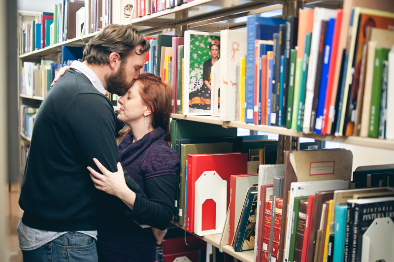 A soon to be groom kisses his bride on the forehead while being photographed in the art section of the State College library.